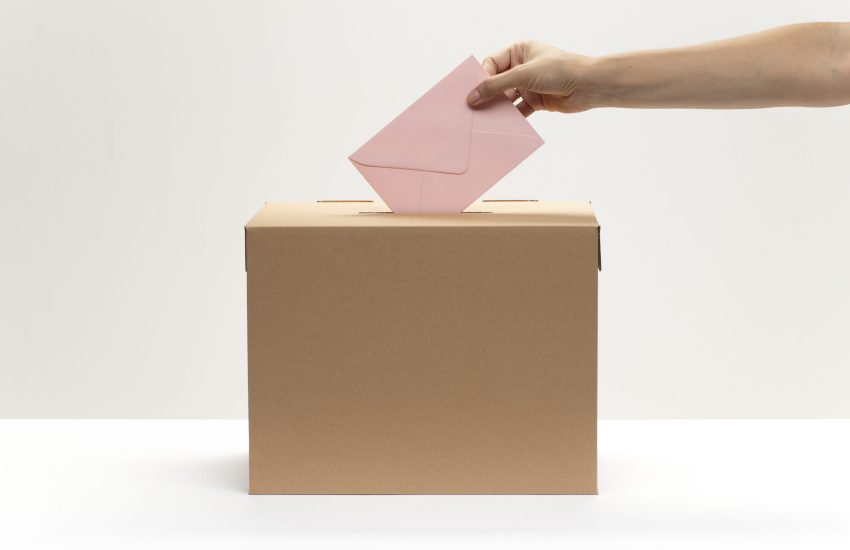 hand-puts-pink-envelope-into-vote-box